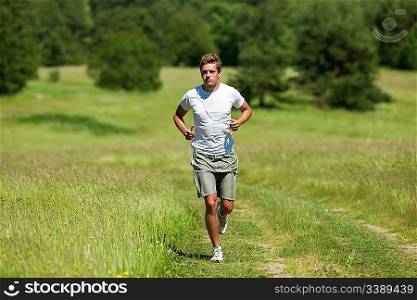 Young man with headphones jogging in a meadow, shallow DOF