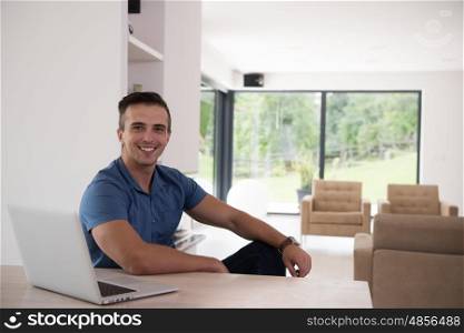 Young man with his laptop computer at his luxury modern home, smiling