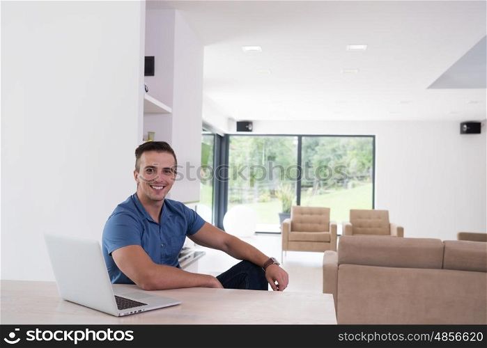Young man with his laptop computer at his luxury modern home, smiling