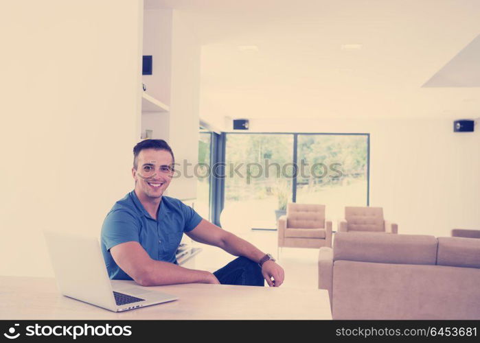 Young man with his laptop computer at his luxury modern home, smiling