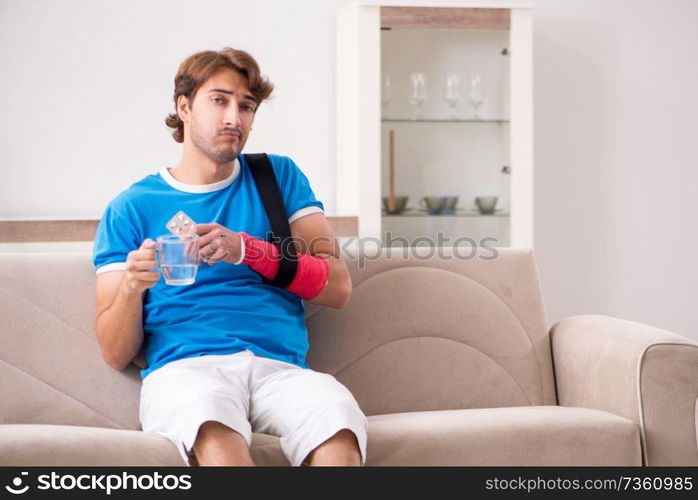 Young man with injured arm sitting on the sofa 