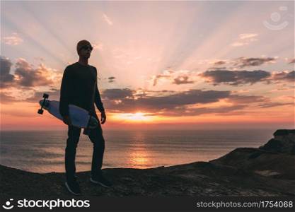 Young man with is skate board watching the sunset