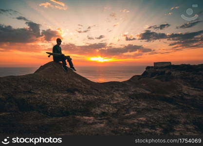 Young man with is skate board watching the sunset