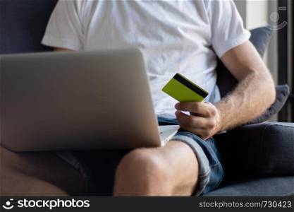 Young man with laptop computer and credit card at home. Shopping and lifestyle concept.