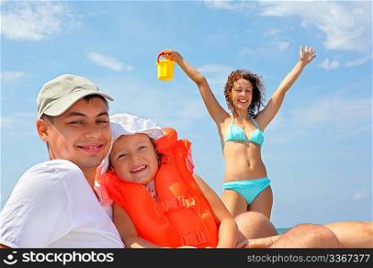 young man with little girl in orange lifejacket and beautiful woman with plastic toy bucket, woman lifted hands upwards