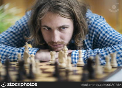 Young man with long hair playing chess game at home. Thinking about his next chess move.. Playing Chess. Man Thinking About His Next Chess Move