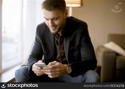 Young man with mobile phone by window in the apartment