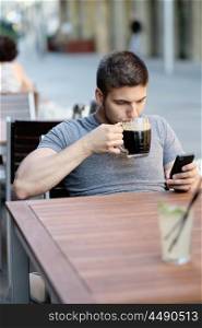 Young man with mobile phone drinking beer in outdoor restaurant