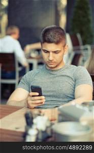 Young man with mobile phone in outdoor restaurant