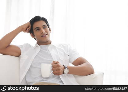 Young man with mug of tea thinking