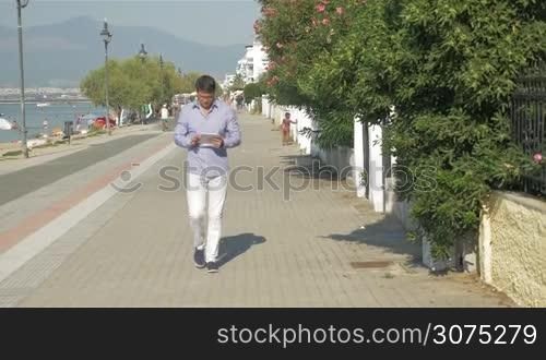 Young man with pad walking on waterfront and leaping with joy as getting good news. Businessman happy with success