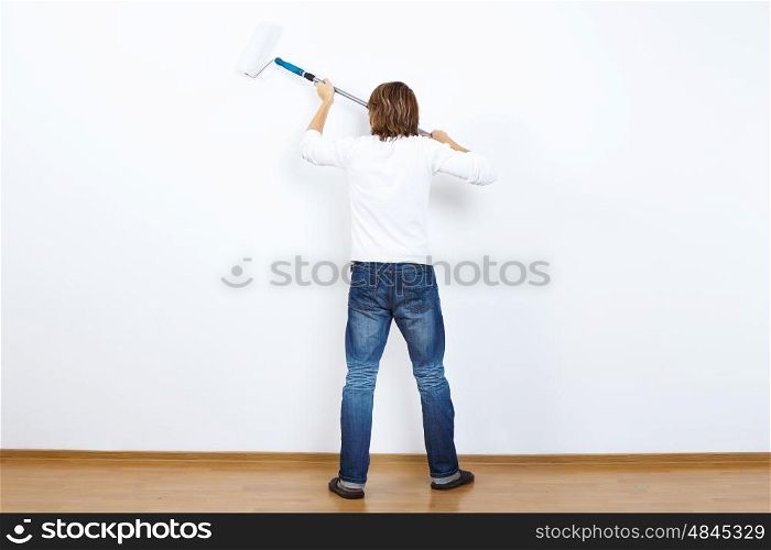Young man with paint brush and blank white wall