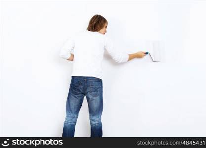 Young man with paint brush and blank white wall