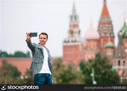 Young man with phone outdoors on background of St Basils Church and Kremlin. Portrait of businessman in Moscow. Happy young urban man in european city.