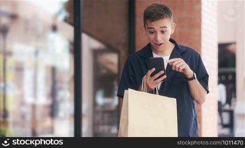 Young man with shopping bags is using a mobile phone while doing shopping