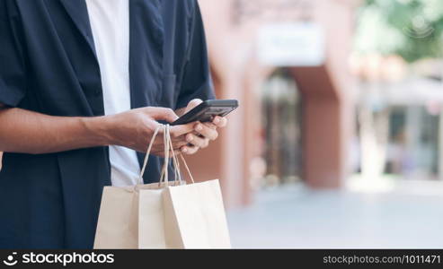 Young man with shopping bags is using a mobile phone while doing shopping.