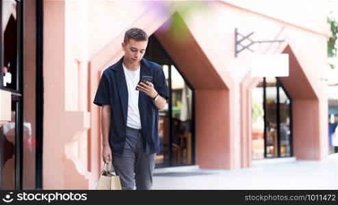 Young man with shopping bags is using a mobile phone while doing shopping.