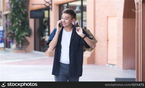 Young man with shopping bags is using a mobile phone while doing shopping.