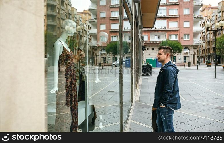 Young man with shopping bags looking at a shop window to buy a gift. Man looking shop window to buy a gift