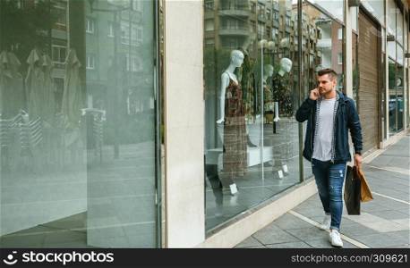 Young man with shopping bags walking in front of a clothing store. Man with shopping bags in front clothing store