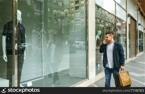 Young man with shopping bags walking in front of a clothing store. Man with shopping bags in front clothing store