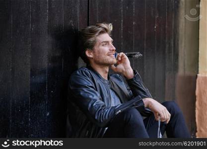 Young man with smartphone earphones sitting in the street black door