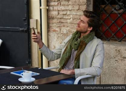 Young man with smartphone in an cafe outdoor sitting having some coffe