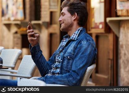 Young man with smartphone smiling in an cafe outdoor sitting