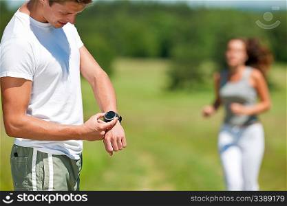 Young man with stopwatch measuring time, woman in background, shallow DOF