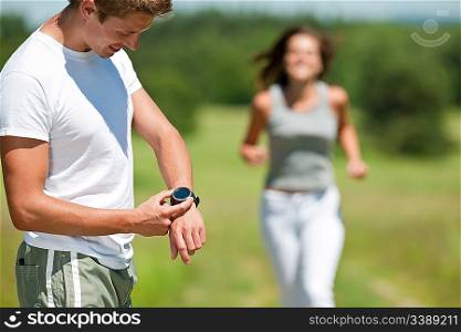 Young man with stopwatch measuring time, woman in background, shallow DOF