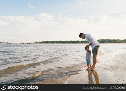 Young man with toddler son looking down at sea, Pelham Bay Park, Bronx, New York, USA