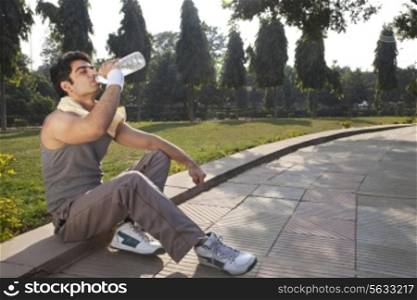 Young man with towel round shoulders drinking water after workout