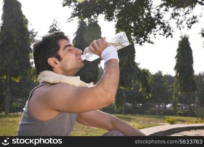 Young man with towel round shoulders drinking water after workout