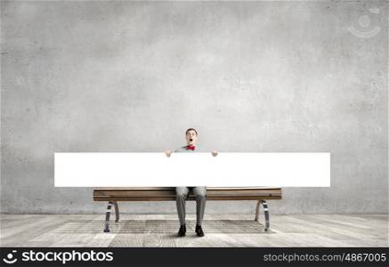 Young man with white blank banner sitting on bench