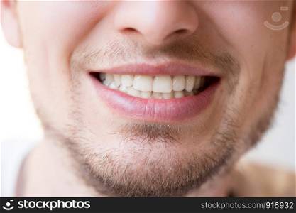 Young man with white teeth, red lips and a beard is smiling