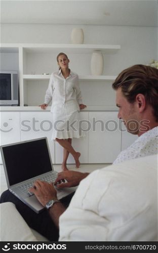 Young man working on a laptop with a young woman standing in front of him