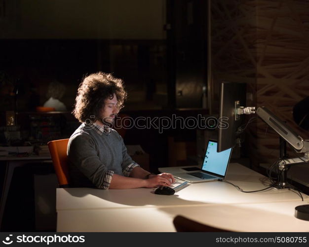 Young man working on computer at night in dark office. The designer works in the later time.