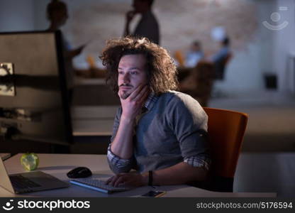 Young man working on computer at night in dark office. The designer works in the later time.