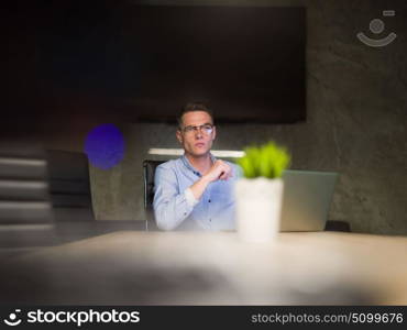 Young man working on laptop at night in dark office. The designer works in the later time.