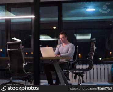 Young man working on laptop at night in dark office. The designer works in the later time.