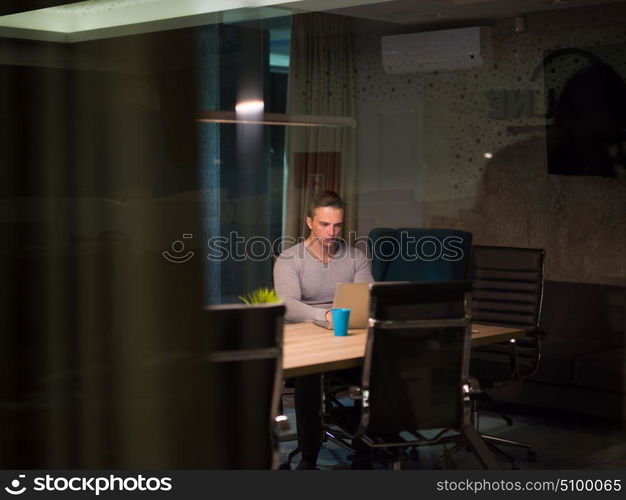 Young man working on laptop at night in dark office. The designer works in the later time.