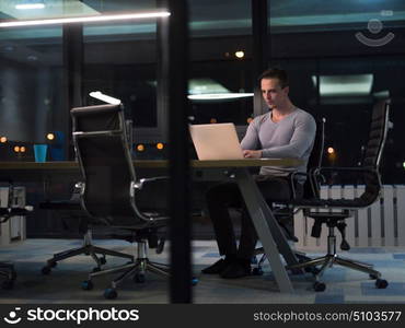 Young man working on laptop at night in dark office. The designer works in the later time.