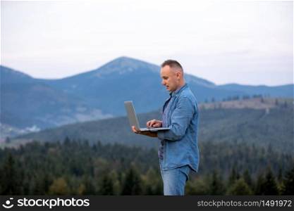 young man working on laptop in the mountains. working online. Cellular network broaband coverage concept.. young man working on laptop in the mountains. working online. Cellular network broaband coverage concept