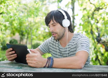 young man working with a tablet pc listening music with headphones on a wooden table, outdoor