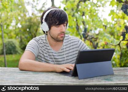 young man working with a tablet pc listening music with headphones on a wooden table, outdoor