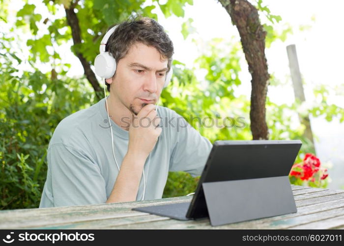 young man working with a tablet pc listening music with headphones on a wooden table, outdoor