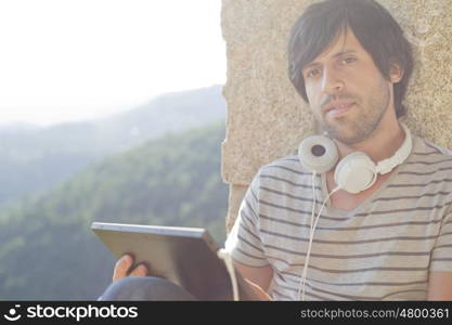 young man working with a tablet pc listening music with headphones, outdoor