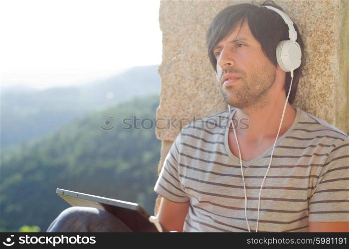young man working with a tablet pc listening music with headphones, outdoor
