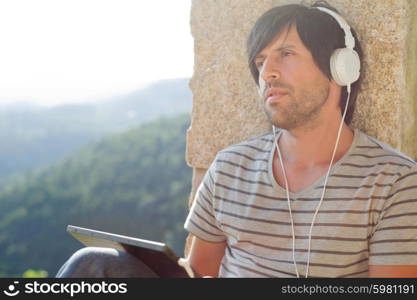 young man working with a tablet pc listening music with headphones, outdoor