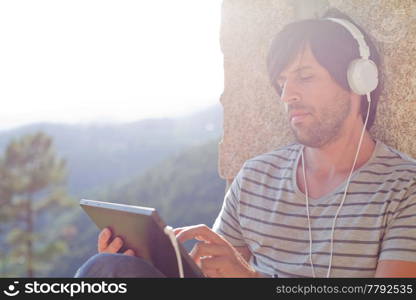 young man working with a tablet pc listening music with headphones, outdoor